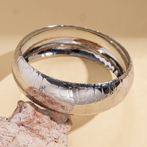 Close-up of a silver metal cuff bracelet featuring a detailed crocodile skin pattern