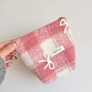 Detail of pink plaid plush makeup bag with bow pattern and golden zipper held in hand
