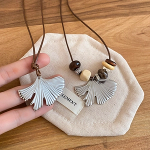 Close-up of stainless steel ginkgo leaf pendants with wood beads on brown leather cord