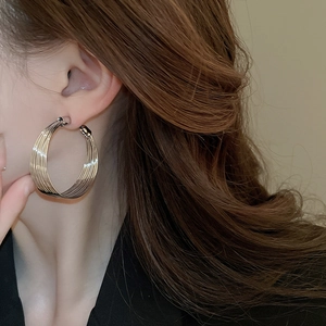 Close-up of model wearing geometric multi-layer hoop earrings in polished metal finish