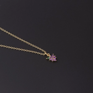 Detail of purple zircon grape pendant on a fine gold chain against dark background