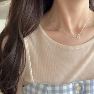 Close-up of a delicate silver bow pendant necklace with zircon stones on a model
