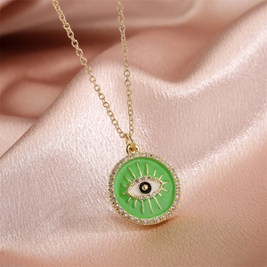 Detail of gold evil eye pendant with green enamel and zircons on pink silk