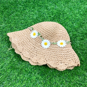 Macro detail of hand-woven straw sun hat with white daisy floral band and wavy brim