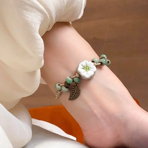 Détail du bracelet tissé main avec fleurs en céramique blanche et perles vertes