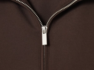 Detailed close-up of the silver metal zipper and high-density fabric on a coffee brown sweatshirt