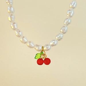 Detailed view of pearl necklace featuring red cherry pendant with green leaves detail