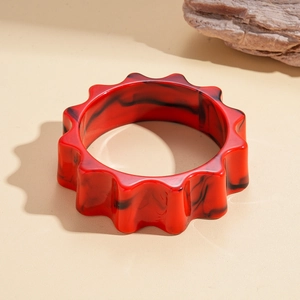 Detail of red and black marbled acrylic gear bangle with artistic wavy edge on stone