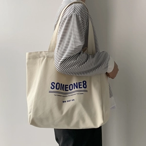 Minimalist cream canvas tote bag with blue lettering shown as a side shoulder carry