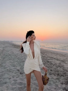 Detail of elegant cream deep V-neck mini dress with ruched waist on a beach background