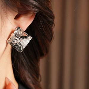 Close-up of geometric square silver earrings with faceted texture on model ear