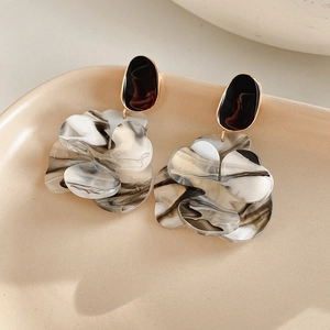 Detail view of large marble resin flower earrings displayed on a cream ceramic tray