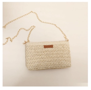 Detail of hand-woven straw crossbody bag with golden chain strap and leather patch