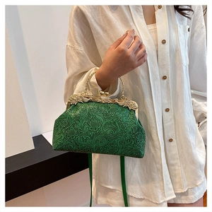 Detail of green shell bag with floral embossing, metal handle and gold chain strap