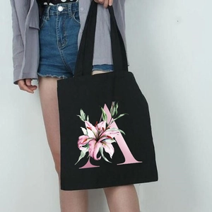 Black canvas tote bag featuring a pink lily flower and letter A print held by a model