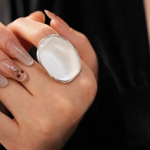 Close-up of a silver ring with a white oval resin stone on a hand with manicured nails
