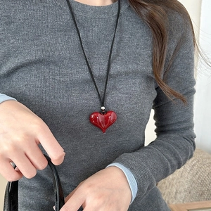 Close-up of a red heart pendant necklace on a grey sweater during daily wear