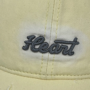 Detailed close-up of grey Heart script embroidery on a pale yellow cotton baseball cap