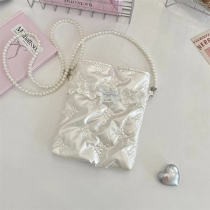 Dettaglio del motivo fiocco trapuntato su borsa in raso bianco con tracolla di perle