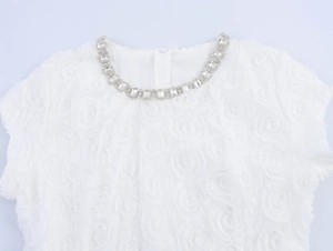 Détail de robe blanche avec texture de roses 3D et décoration en cristal au décolleté
