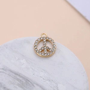 Gold-plated peace sign charm with crystals on a marble tray for DIY jewelry projects