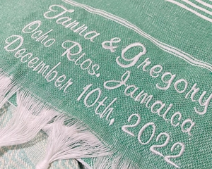 Close-up of custom white embroidery on green striped Turkish beach towel with tassels