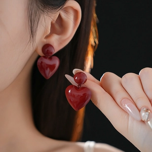 Close-up of minimalist red heart pendant earrings worn by a model in deep red gloss
