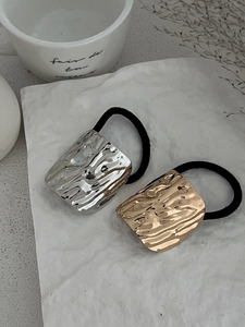 Close-up of gold and silver hammered metal charms on black elastic ponytail holders