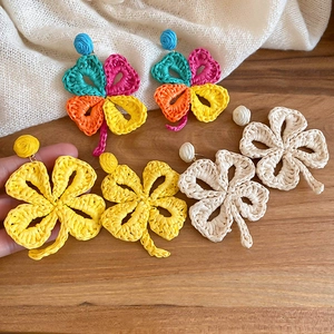 Detail showing colorful handmade raffia woven clover earrings on a rustic wood background