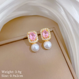 Detail of gold drop earrings with pink oval gemstone and white pearl on beige velvet