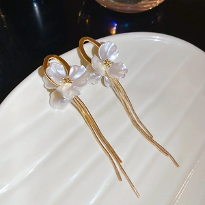 Close-up of pearl flower earrings with gold chain tassels on white wavy plate