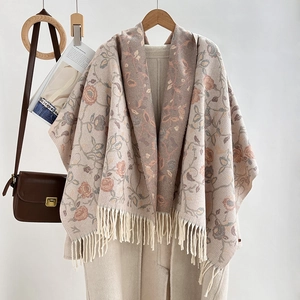 Detail of beige and pink floral knit scarf with tassel fringe on wooden hanger
