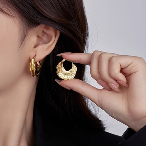 Detail showing wavy textured 18K gold irregular hoop earrings on a model's ear