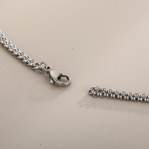 Détail d'un collier chaîne gourmette argentée avec fermoir mousqueton et texture métallique