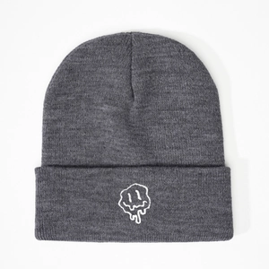 Close-up of the white melting smiley face embroidery on a dark grey knitted beanie
