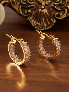 Macro detail of 18k gold plated hoop earrings with pink zirconia stones on a wooden background