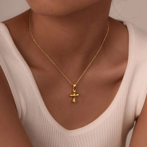 Close-up of a minimalist gold cross pendant with liquid metal texture on a female model