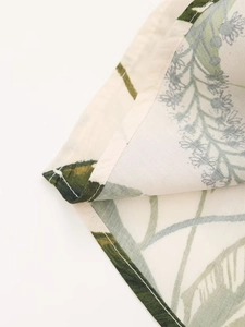 Detail of cotton linen fabric showing flat seam stitching and green floral leaf patterns