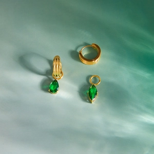 Primo piano di orecchini d'oro con trama verticale e pendenti in zircone verde