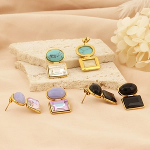 Close-up of geometric square earrings with natural stones on elegant silk fabric