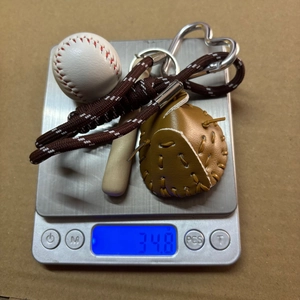 Mini baseball keychain set weighing 34.8g with bat, glove, and heart clasp on a scale