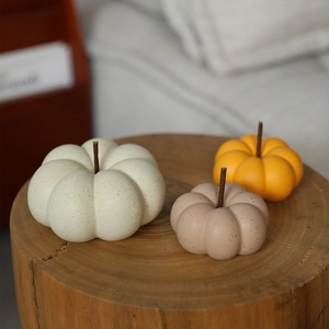 Three creative ceramic pumpkin ornaments in cream, oat and orange on a wood stump