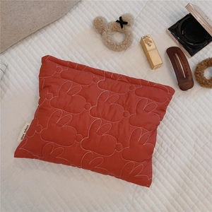 Macro view of red quilted cosmetic bag with white rabbit stitching and brand label