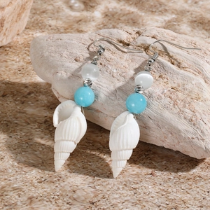 Detail of bohemian drop earrings with natural shells and blue beads on a textured rock