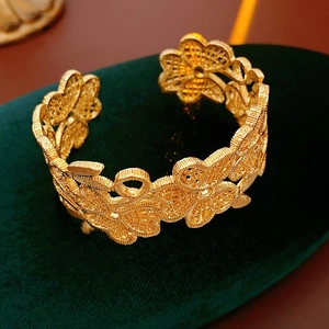 Detail eines vergoldeten, floralen Armreifs mit Hohlmuster auf grünem Samtständer