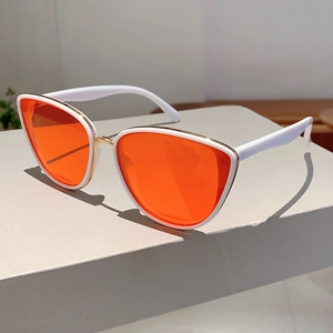 Detail view of white cat-eye sunglasses with orange lenses and golden metal bridge