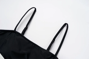 Detail of black one-piece swimsuit featuring adjustable spaghetti straps and metal buckles