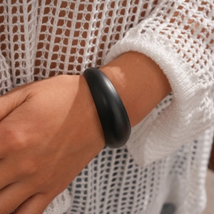 Close-up of minimalist black matte acrylic bangle on model with soft lighting