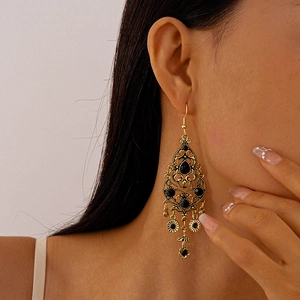 Close-up of vintage gold hollow earrings with black teardrop rhinestones on a model