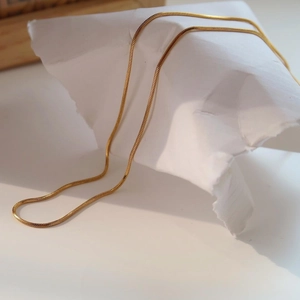 Close-up of golden titanium steel snake chain necklace on white paper display